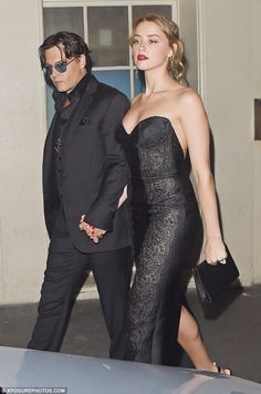 a woman in a black dress walking next to a man in a suit and tie