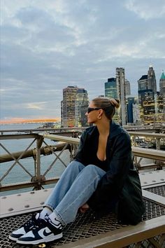 a woman sitting on top of a wooden bench next to the ocean and city skyline