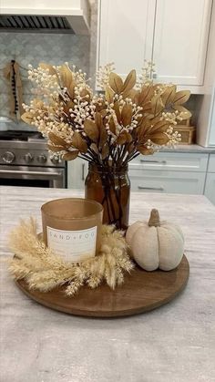 a wooden plate topped with a vase filled with dried flowers and a candle on top of it