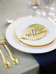 a white plate topped with a gold leaf next to two silver forks and knifes