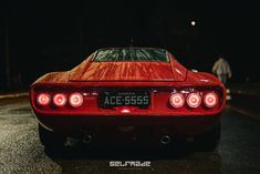 a red sports car parked on the side of the road at night with its lights on