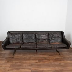 a brown leather couch sitting on top of a hard wood floor next to a white wall