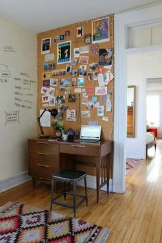 a desk with a laptop on it in front of a corkboard wall covered with pictures