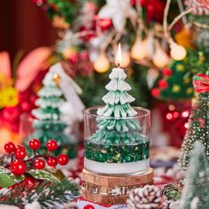 a lit candle sitting on top of a table next to christmas decorations and trees in the background