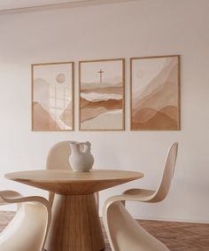 three paintings hang on the wall above a round table with two chairs and a vase