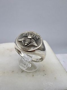 a silver ring sitting on top of a white marble block with a coin in the middle