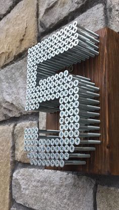 there is a metal letter made out of screws on a brick wall with a wooden frame