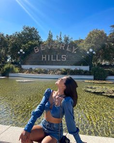 a woman sitting on the edge of a fountain in front of beverly hills sign