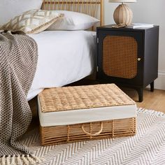 a wicker chest sitting on top of a bed next to a night stand and lamp