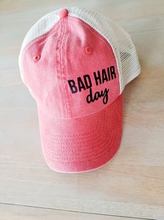 a pink hat with the words bad hair day on it sitting on a wooden surface