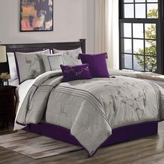 a bed with purple and grey comforters in a room next to a window,