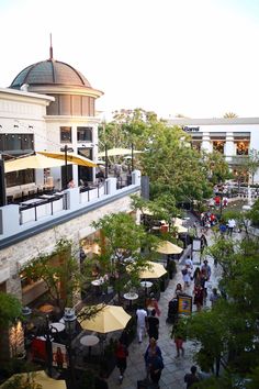 an overhead view of people sitting at tables and umbrellas in a courtyard with trees