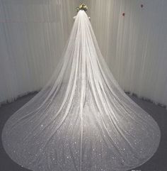 a white wedding veil with flowers on top is hanging in front of a curtained wall