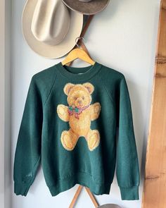 Retro 80's Brown Holiday Teddy Bear with Gold Sparkle Details on a Green Sweater.  Ladies Medium Ugly Bear Christmas Sweatshirt.  Cotton/poly. Fruit of the Loom. USA. Length: 23.5" Underarm to Underarm: 22".Check out the rest of our shop: https://instagram.com/hollyshopvintage?igshid=OGQ5ZDc2ODk2ZA== https://hollyshopvintage.etsy.com/ Orders over $35 ship for free. Please check out my Instagram for my newest finds: Hollyshopvintage  Everything priced over $35 has shipping already included in the total price. I'll gladly combine shipping on multiple items to save you money, when it is safe to do so! Message me to make adjustments ahead of time, or make your purchase and I'll refund the shipping overages.  Most items are Vintage. Expect some vintage wear. Items may contain unmentioned flaws. Teddy Bear Sweatshirt, Bear Clothing, Teddy Collections, Bear Christmas, Bear Outfits, New Braunfels, Gold Sparkle, Green Sweater, Vintage Wear