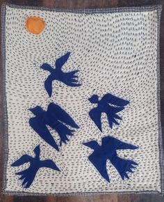 three blue birds flying in the air on a white and black cloth with an orange dot