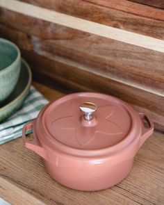 a pink casserole sitting on top of a wooden table next to a green bowl