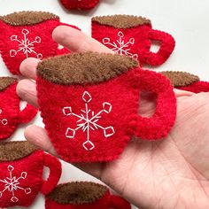 a hand holding a red cup with white snowflakes on it and some brown felt cups