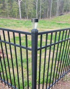 a black metal fence with a light on it's top and grass in the background