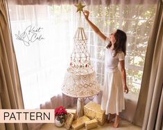 a woman decorating a christmas tree in front of a window with white sheer curtains