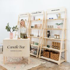 a woman standing behind a table with candles and plants on it in front of shelves