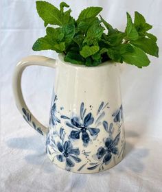 a blue and white flower pot with green leaves in it on a white cloth background