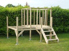 a wooden structure sitting in the grass next to a bush and some bushes with ladders on each side