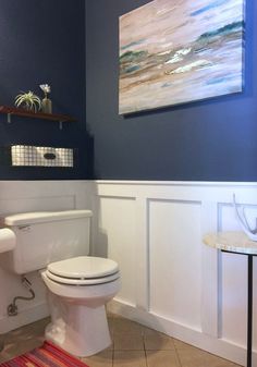 a white toilet sitting next to a sink in a bathroom under a painting on the wall