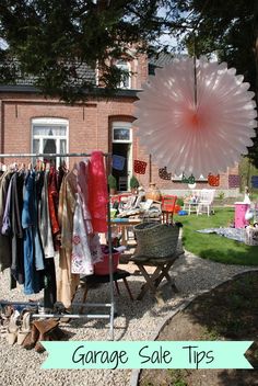 clothes are hung on racks in front of a house with lawn chairs and an umbrella