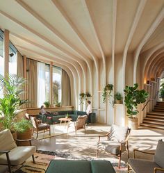 a living room filled with lots of furniture next to tall windows and potted plants