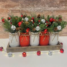 three mason jars filled with pine cones and red balls are tied to a wooden tray