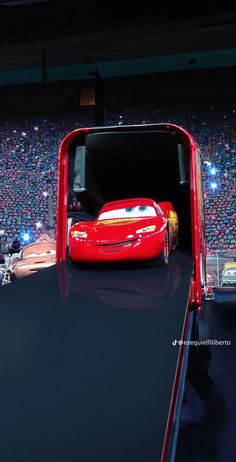 a red car is parked in front of an audience at a movie theater with cars coming out from the back