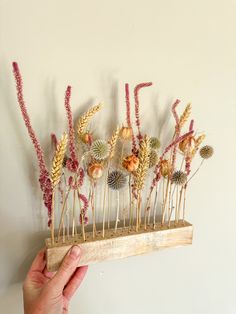 a hand is holding a wooden stick with dried flowers on it and the sticks are made out of wood