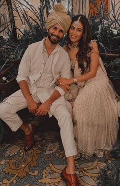 a man and woman sitting next to each other on a bench in front of plants