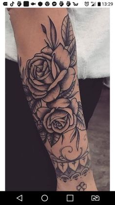 a woman's arm with roses on it and leaves in the middle, while she is wearing a white t - shirt