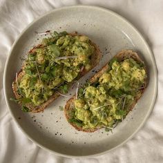 two pieces of bread topped with guacamole on top of a white plate