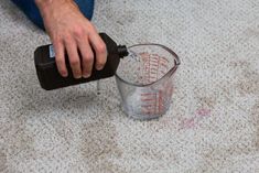 a man is pouring something into a measuring cup on the floor with his hands and feet