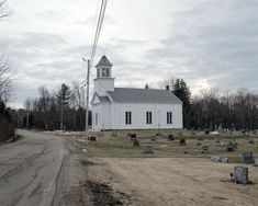 an old white church sits in the middle of a field with tombstones and trees