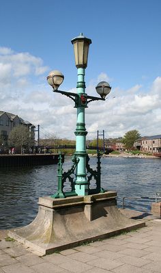 a street light sitting on the side of a river next to a sidewalk and lamp post