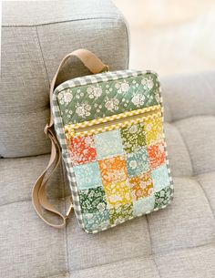 a multicolored patchwork purse sitting on top of a gray couch next to a pillow