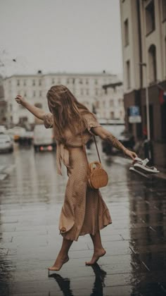 a woman is walking down the street in the rain with an umbrella and handbag