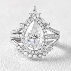 a white diamond and pearl ring on top of a white cloth covered table with pearls