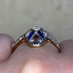 An elongated diamond and sapphire ring from the Edwardian era. The center stone is a bezel-set old European cut diamond with a weight of approximately 0.15 carats. The center diamond is accented by rows of calibre cut sapphires that are set diagonally across the mounting. The total weight of the sapphires is approximately 0.36 carats. Single and rose cut diamonds are set around the edges of the openwork mounting and along the shoulders. The total weight of the additional diamonds is approximatel Art Deco Yellow Gold Diamond Ring With Bezel Setting, Antique Oval Sapphire Ring With Single Cut Diamonds, Blue Art Deco Diamond Ring With Rose Cut, Art Deco Blue Diamond Ring With Rose Cut, Anniversary Sapphire Diamond Ring With Rose Cut, Victorian Sapphire Ring With Diamond For Formal Occasions, Formal Victorian Sapphire Ring Accented With Diamonds, Heirloom Sapphire Diamond Ring With Rose Cut, Art Deco Blue Diamond Ring With Single Cut Diamonds