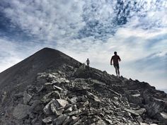 two people walking up the side of a rocky mountain on top of a large pile of rocks