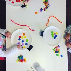 two children at a table with paper plates and crafting supplies on it, one child is holding a plastic fork