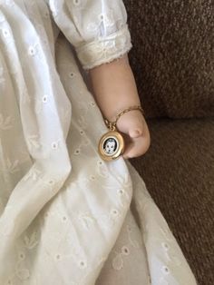 a doll's hand is holding onto the arm of a chair with a white dress on it