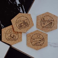 four coasters with different logos on them sitting on a marble counter top next to a black and white tile floor