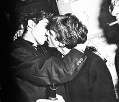 two young men are kissing each other in front of a wall with writing on it