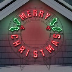 a lighted merry christmas sign on the side of a brick building with green and red lights