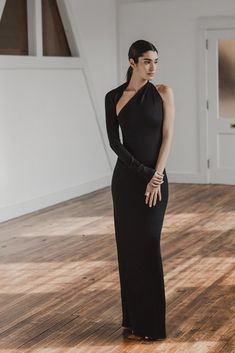 a woman in a long black dress standing on a wooden floor with her hands behind her back