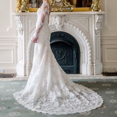 a woman standing in front of a fire place wearing a wedding dress with long sleeves